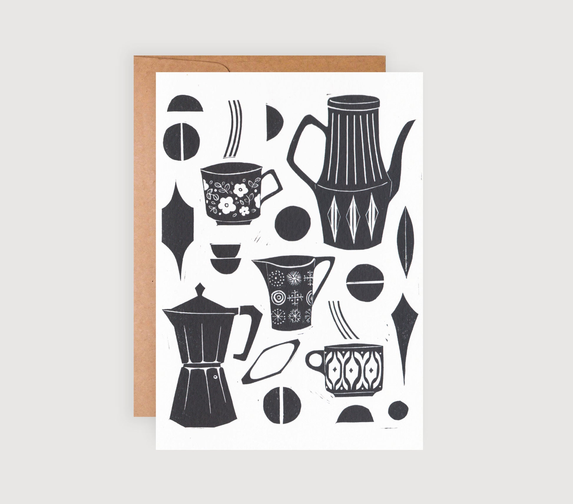A black and white linocut greetings card with coffee-related designs, such as coffee pots and cups, and a brown kraft envelope.