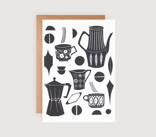 A black and white linocut greetings card with coffee-related designs, such as coffee pots and cups, and a brown kraft envelope.