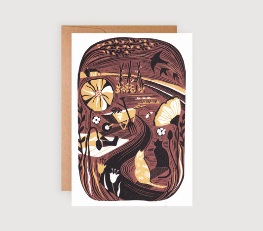 A greetings card featuring a lino print illustration of a garden scene with warm golden tones, depicting plants, veg and cats