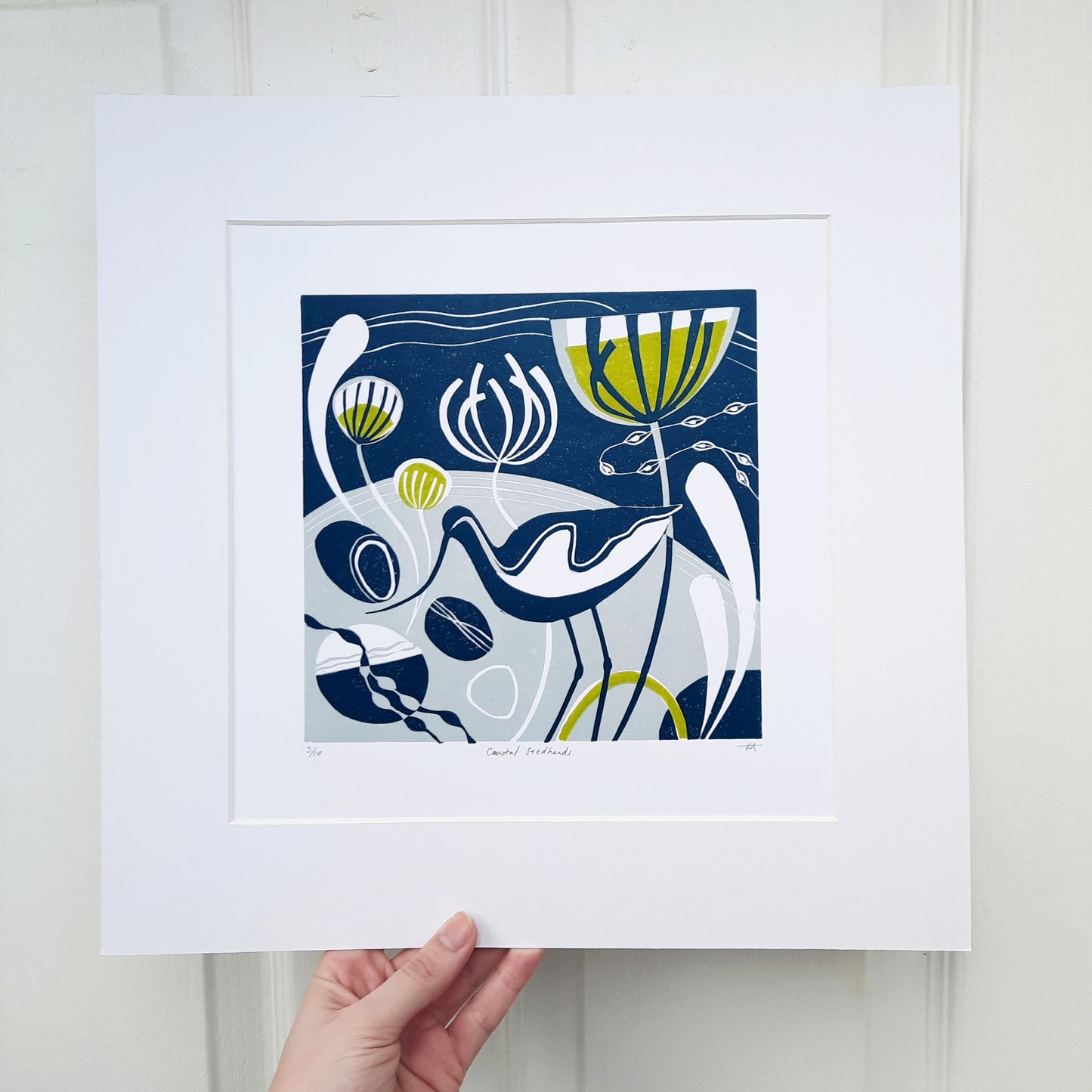 Original lino print featuring an avocet amongst stylised foliage on a shoreline, framed in a white mount.