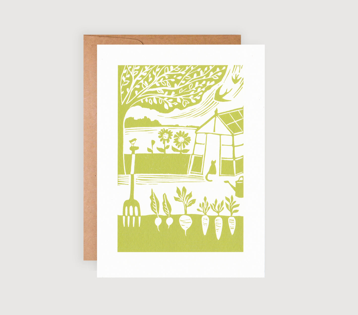 A greetings card with a green linocut print of a garden and a greenhouse, accompanied by a brown kraft envelope.