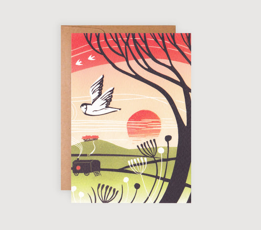 A greetings card featuring a linocut print with a sunset, tree, owl, and a small shepherds hut in an autumnal landscape.