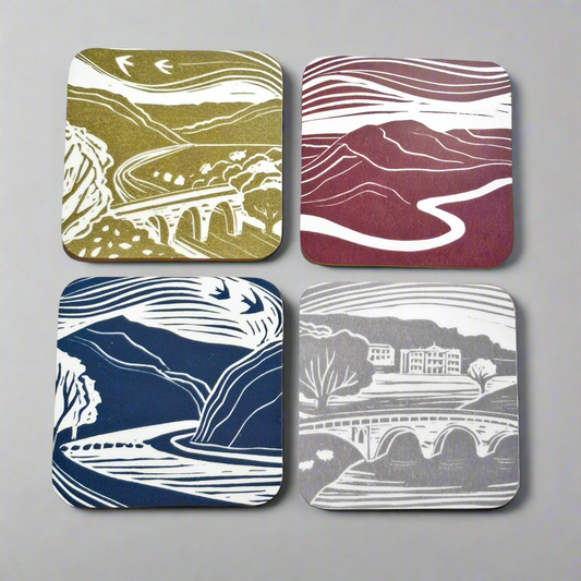 Four square coasters with landscape designs on a gray background