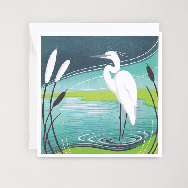 A greeting card featuring a white egret in a reedbed with blue and green tones in the background. The card is square and includes a white envelope.
