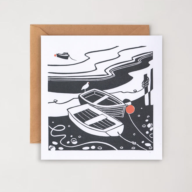 A greetings card with a black and white linocut print of boats on a harbour, accompanied by a brown kraft envelope.