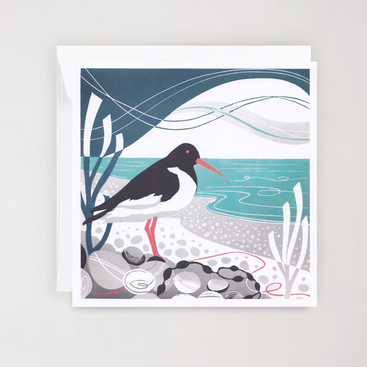 A greetings card featuring a linocut print of an Oystercatcher bird perched on pebbles by the sea, with abstract seascape in the background.