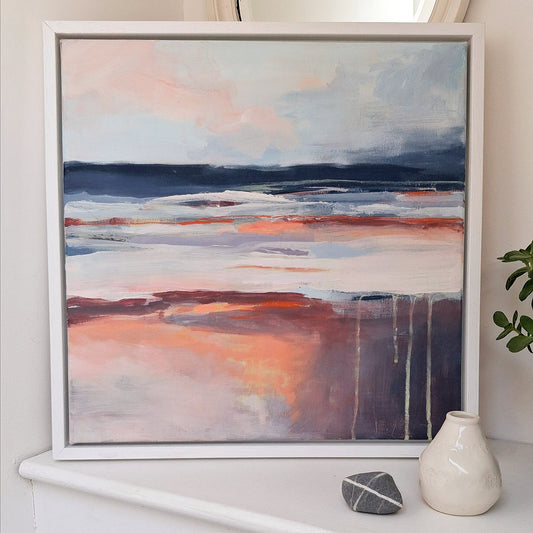 An abstract mixed media canvas painting titled Dawn Horizon, featuring a seascape in shades of white, blue, and orange, framed in a white frame, displayed on a shelf with a decorative vase beside it.