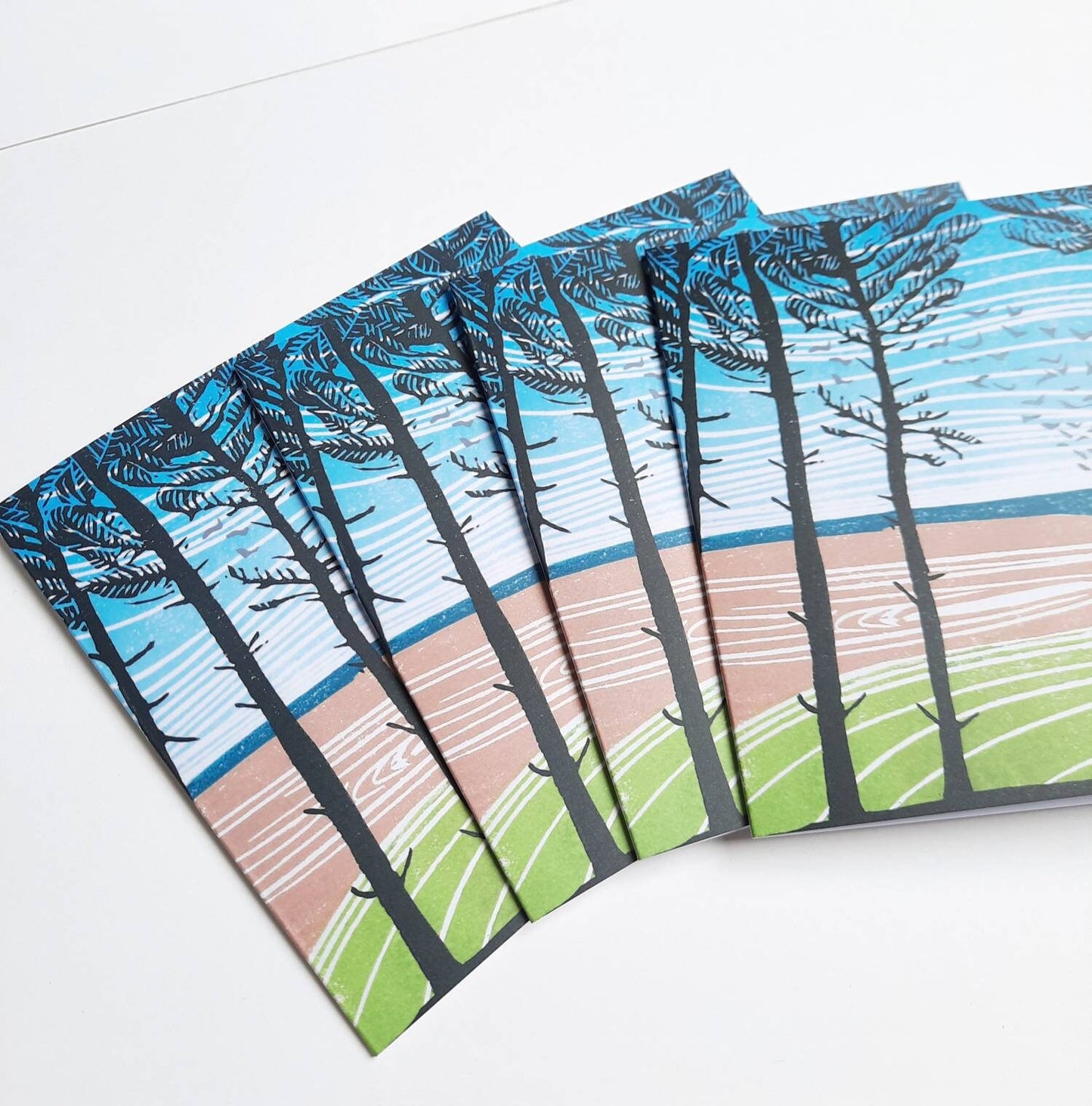 A stack of identical greetings cards featuring a linocut print with pine trees and a landscape.