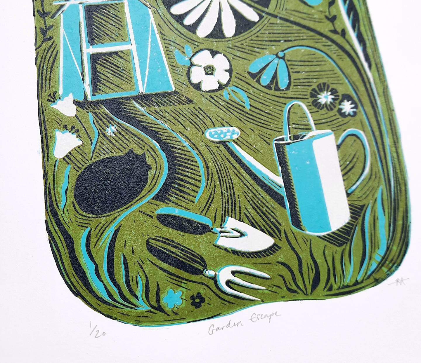 close up of gardening lino print with cat, watering can and tools in the foreground.